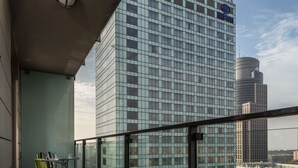 A high-rise building with a glass facade, a balcony with a table and chairs, and a clear view of the surrounding cityscape. - Chopin Apartments Platinum Towers (Warsaw)