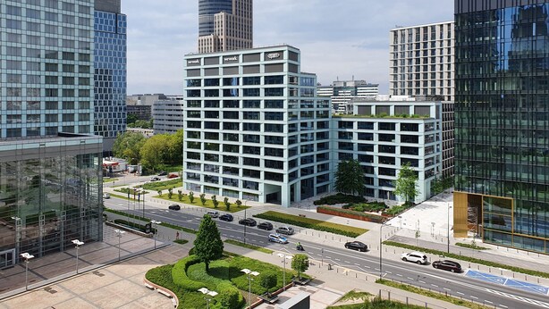 A modern building with a glass facade, surrounded by other high-rise buildings, featuring a central courtyard with greenery and a clear sky. - Chopin Apartments Platinum Towers (Warsaw)
