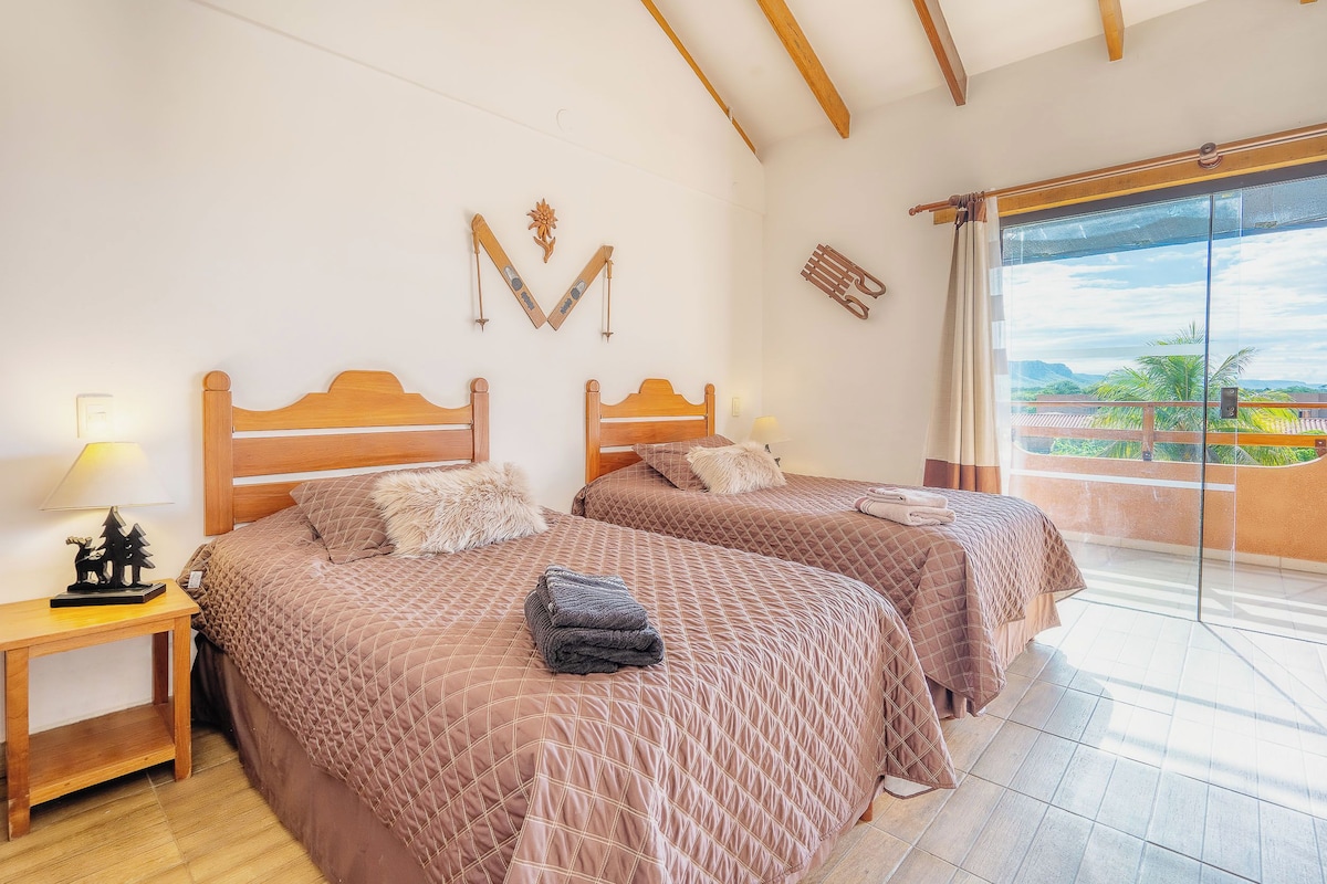 A bedroom with two beds, wooden headboards, a nightstand, and a view of the outdoors.