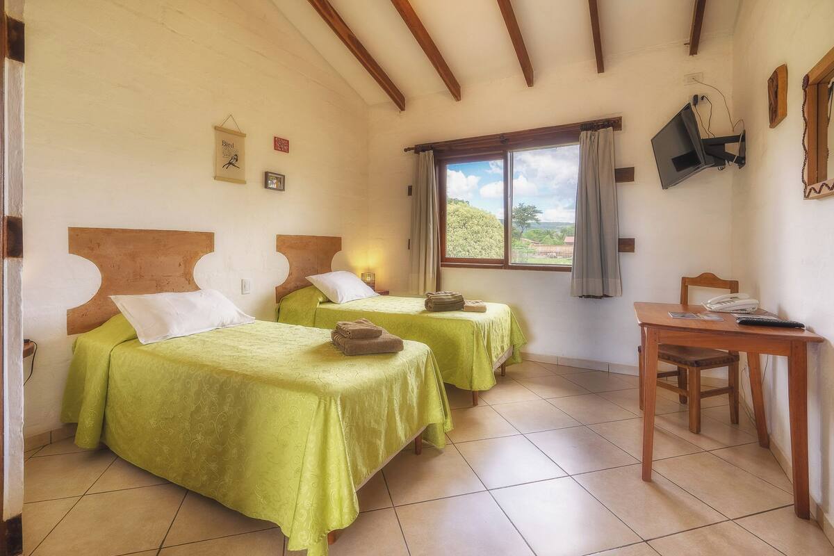 A room with two beds, a desk, a chair, a television, and a window with curtains.