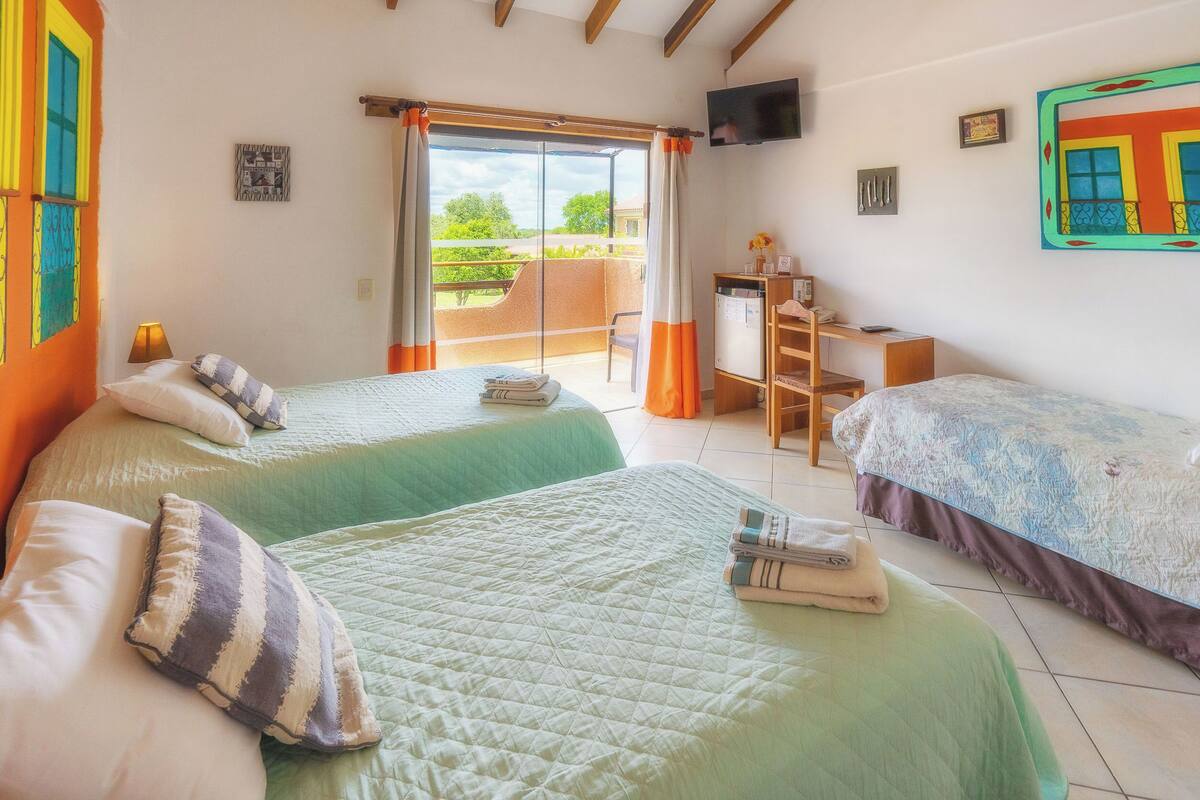 A hotel room with two beds, a desk, a chair, a TV, and a balcony with a view.