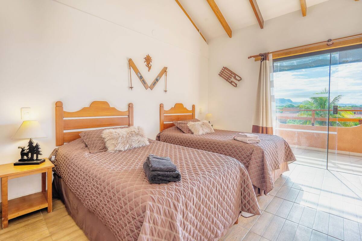 A bedroom with two beds, wooden headboards, a nightstand, and a view of the outdoors.