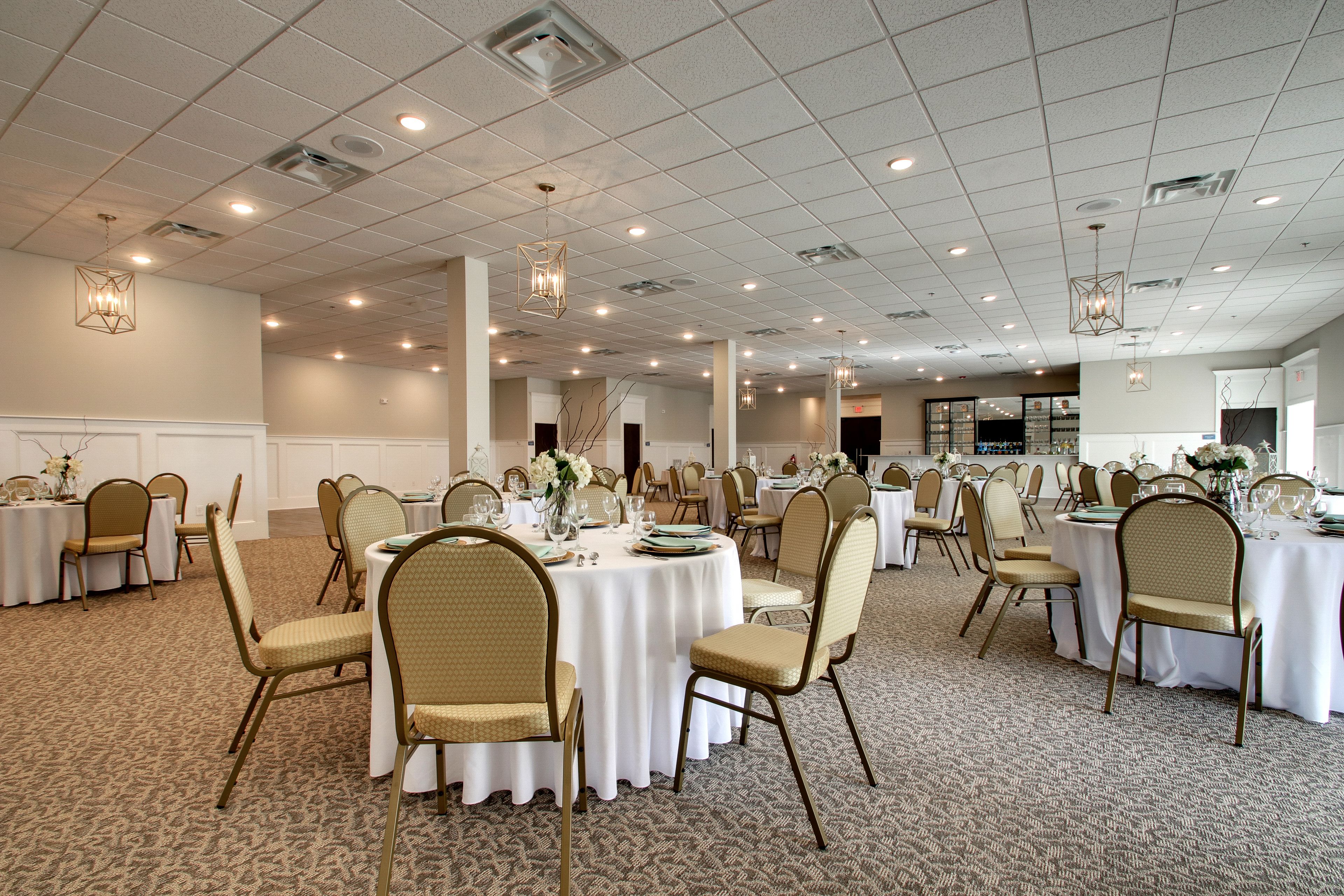Un amplio salón de banquetes con mesas redondas, sillas color beige y manteles blancos.