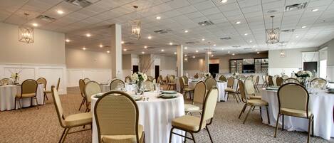 A spacious banquet hall with round tables, beige chairs, and white tablecloths.