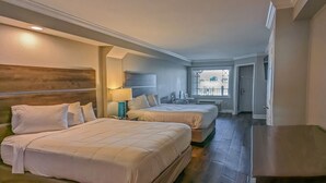 A hotel room with two beds, a desk, a lamp, and a view of the outside. - Islander Hotel & Resort (Emerald Isle)