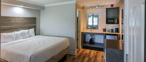A bedroom with a large bed, a wooden headboard, a built-in desk with a mirror, and a kitchenette area.