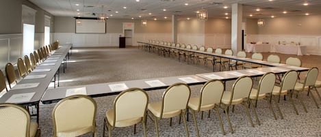A conference room with a long table, rows of chairs, a projector screen, and a podium.