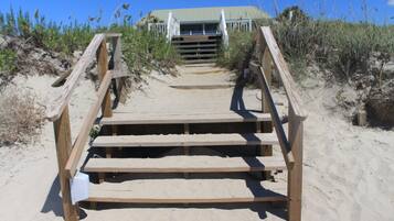 A wooden staircase leading to a building with a green roof, surrounded by sand and sparse vegetation.
