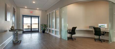 A spacious hallway with a wooden floor, a desk with a computer, and a potted plant.