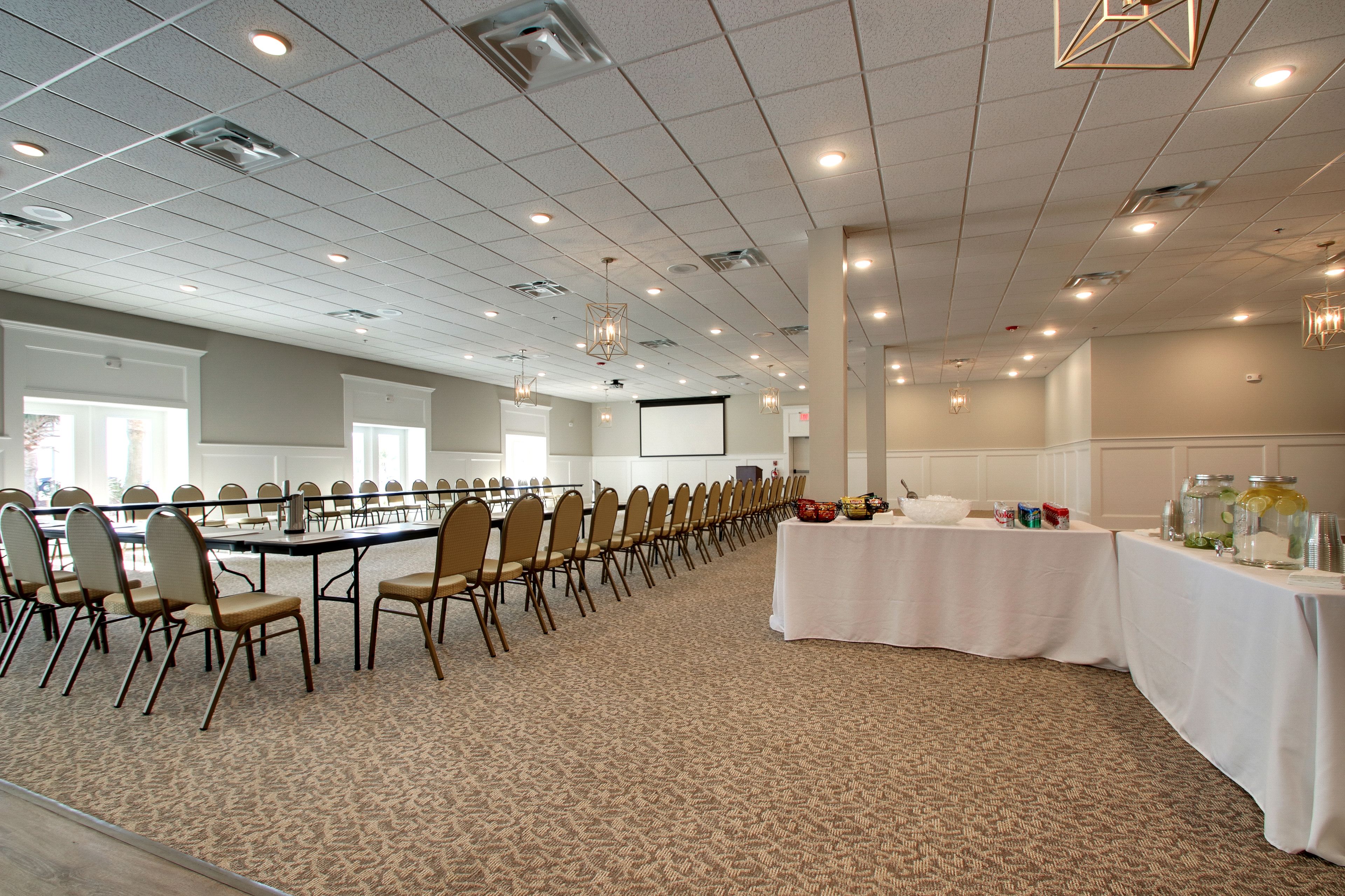 A conference room with rows of chairs, a projector screen, and a table with refreshments.