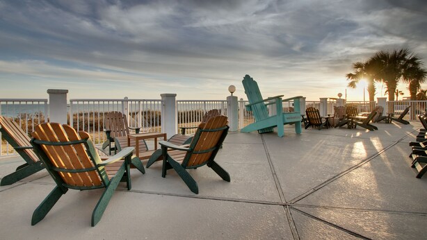 A deck with Adirondack chairs and a table, overlooking the ocean. - Islander Hotel & Resort (Emerald Isle)