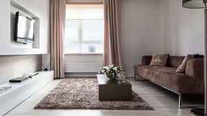 En moderne stue med et fladskærms-tv, en sofa, et sofabord med blomster og et stort vindue med gardiner.