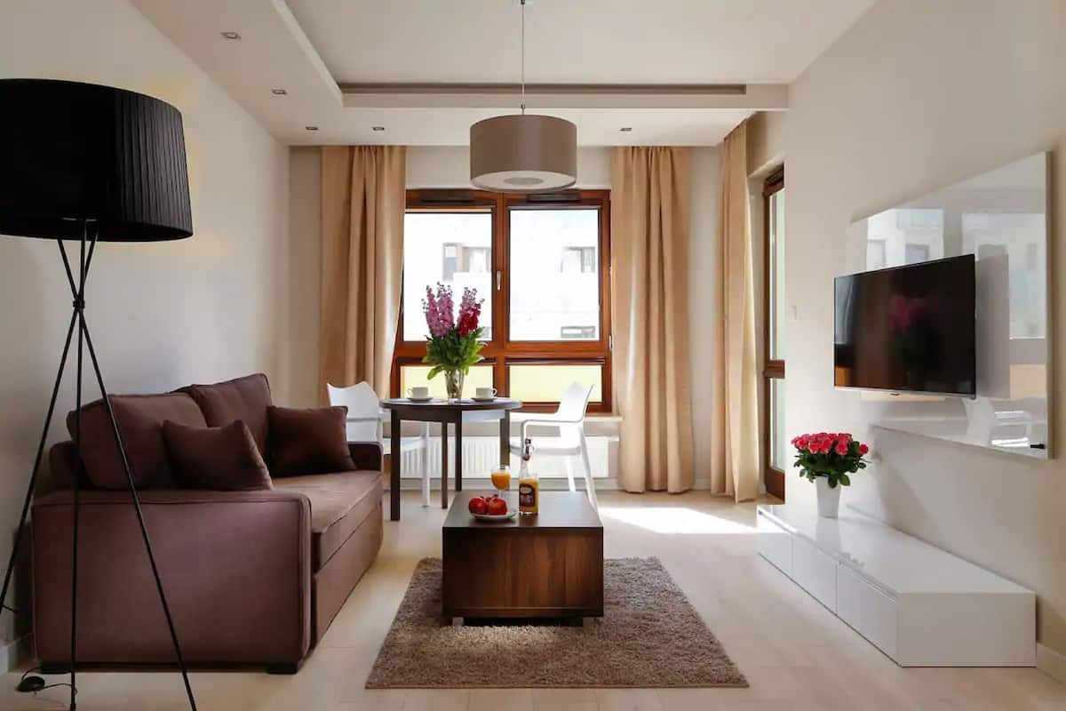 Una sala de estar moderna con un sofá marrón, una mesa de centro, un televisor y un comedor con una mesa y sillas.