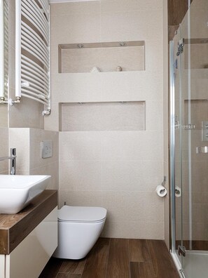A modern bathroom with a white toilet, a glass shower enclosure, and a wooden vanity with a sink. - Chopin Apartments Capital (Warsaw)
