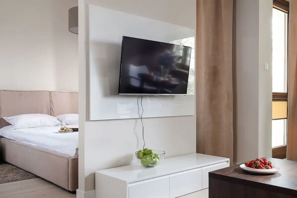 A modern hotel room with a bed, a TV mounted on the wall, a white console table, and a window with curtains. - Chopin Apartments Capital (Warsaw)