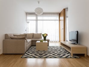 Un soggiorno moderno con un divano beige, un tavolino con un vaso di fiori, una TV a schermo piatto su un supporto e un tappeto decorato.