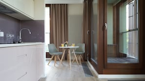 Una cucina moderna con piano cottura integrato, lavello e finestra con tende. C'è un'area pranzo con tavolo, due sedie e una finestra con vista all'esterno.