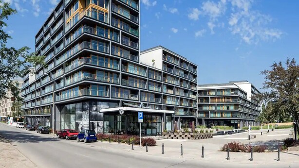 A modern multi-story building with a glass facade, a covered entrance, and a parking area. - Chopin Apartments City (Warsaw)