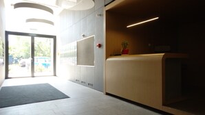 A reception area with a reception desk, a potted plant, and a large window with a view of the outside. - Chopin Apartments City (Warsaw)