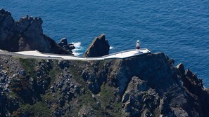 A coastal road with a white road surface, a rocky cliff, and a lighthouse. - Muiño das Cañotas (Carino)