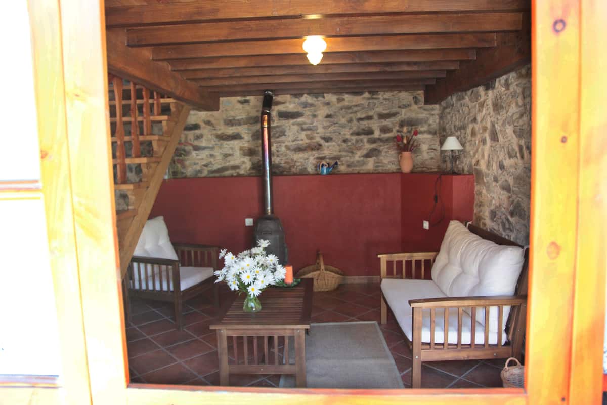 A cozy room with a stone wall, wooden furniture, a fireplace, and a staircase.