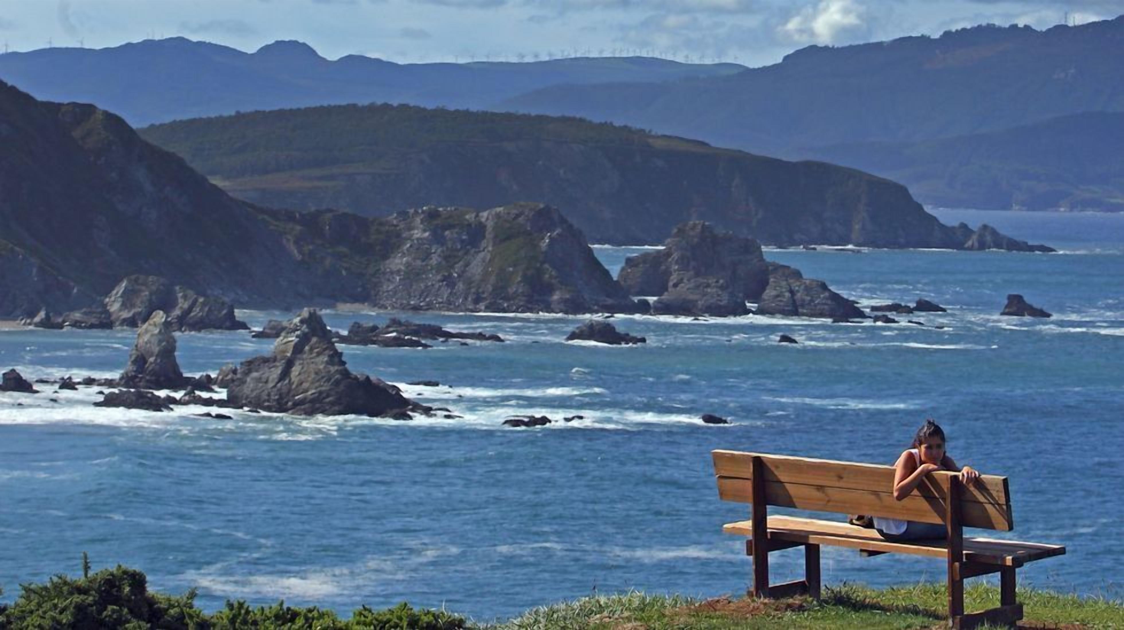 Una banca amb vista a la costa, amb roques i mar a la vista.
