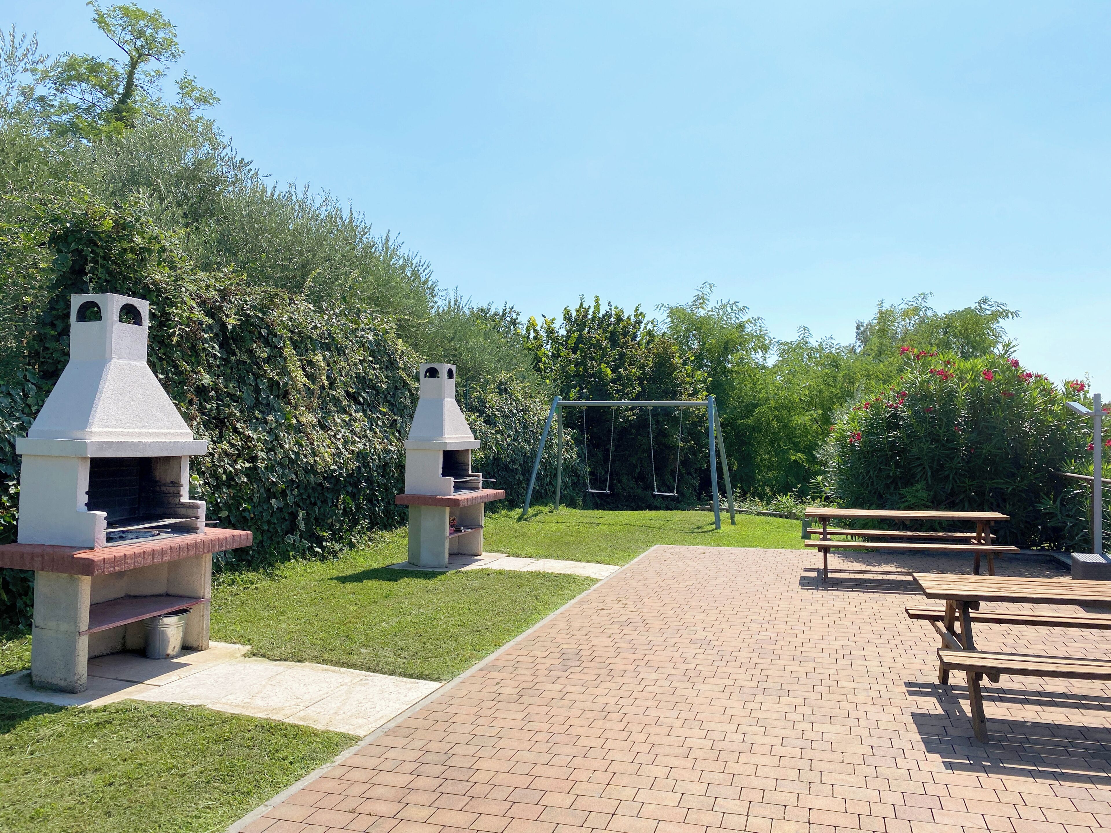 A patio area with two barbecue grills, a swing set, and picnic tables.