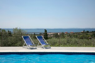 Piscina con due sdraio blu e vista sul mare e colline in lontananza.