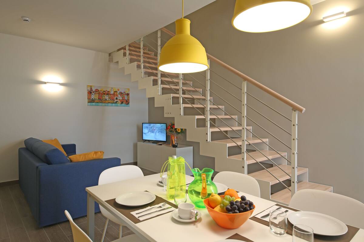 A modern living room with a dining area, a staircase, and a television.