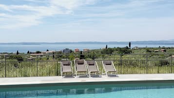 A clear pool with lounge chairs and a view of the sea and distant hills.