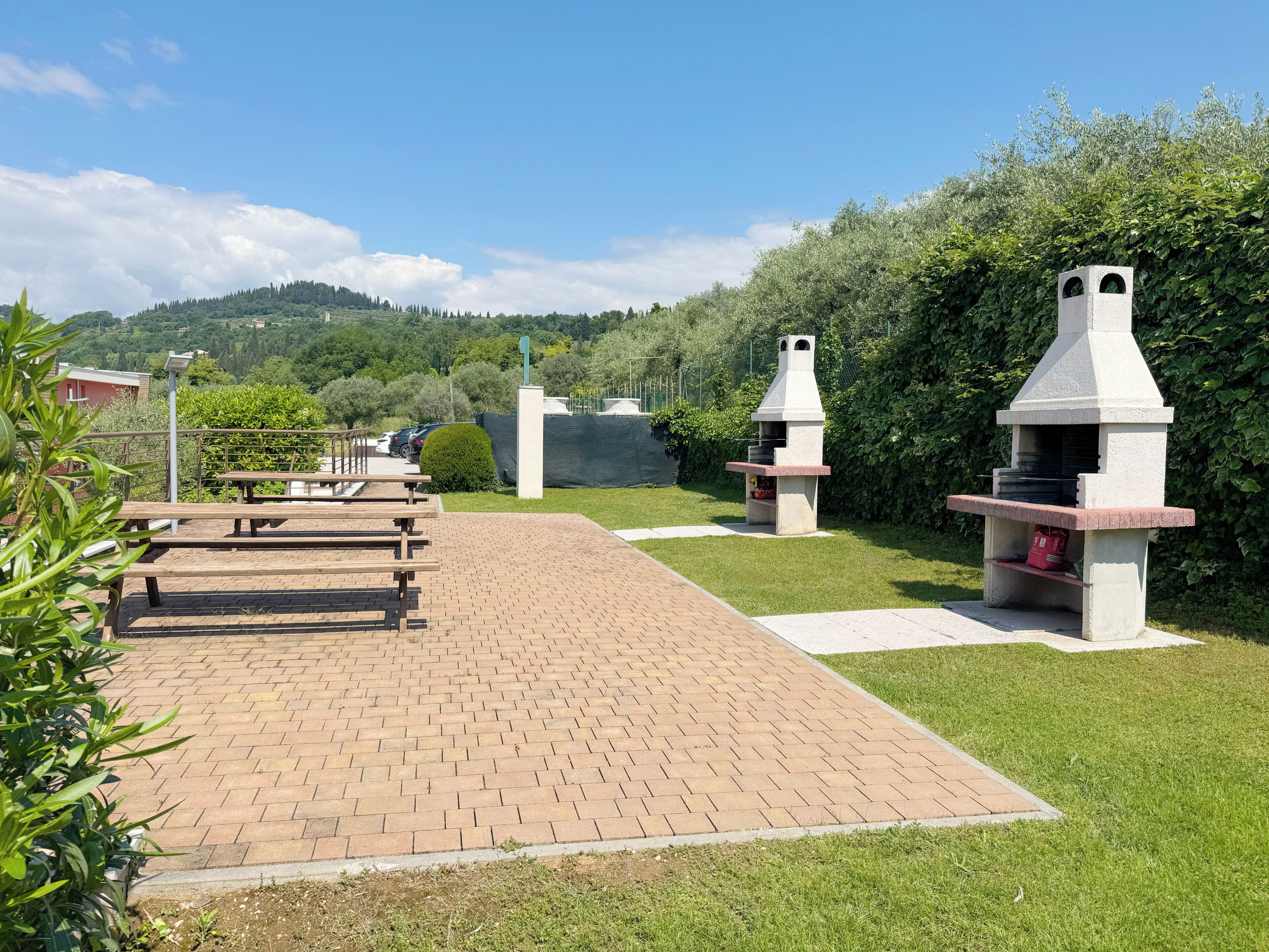 Um espaço de pátio pavimentado com mesas de piquenique e duas churrasqueiras ao ar livre.