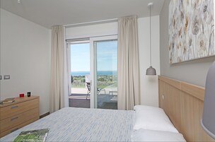 Una camera d'albergo con un letto, una cassettiera in legno, una scrivania con una sedia e vista sull'esterno tramite una porta scorrevole.