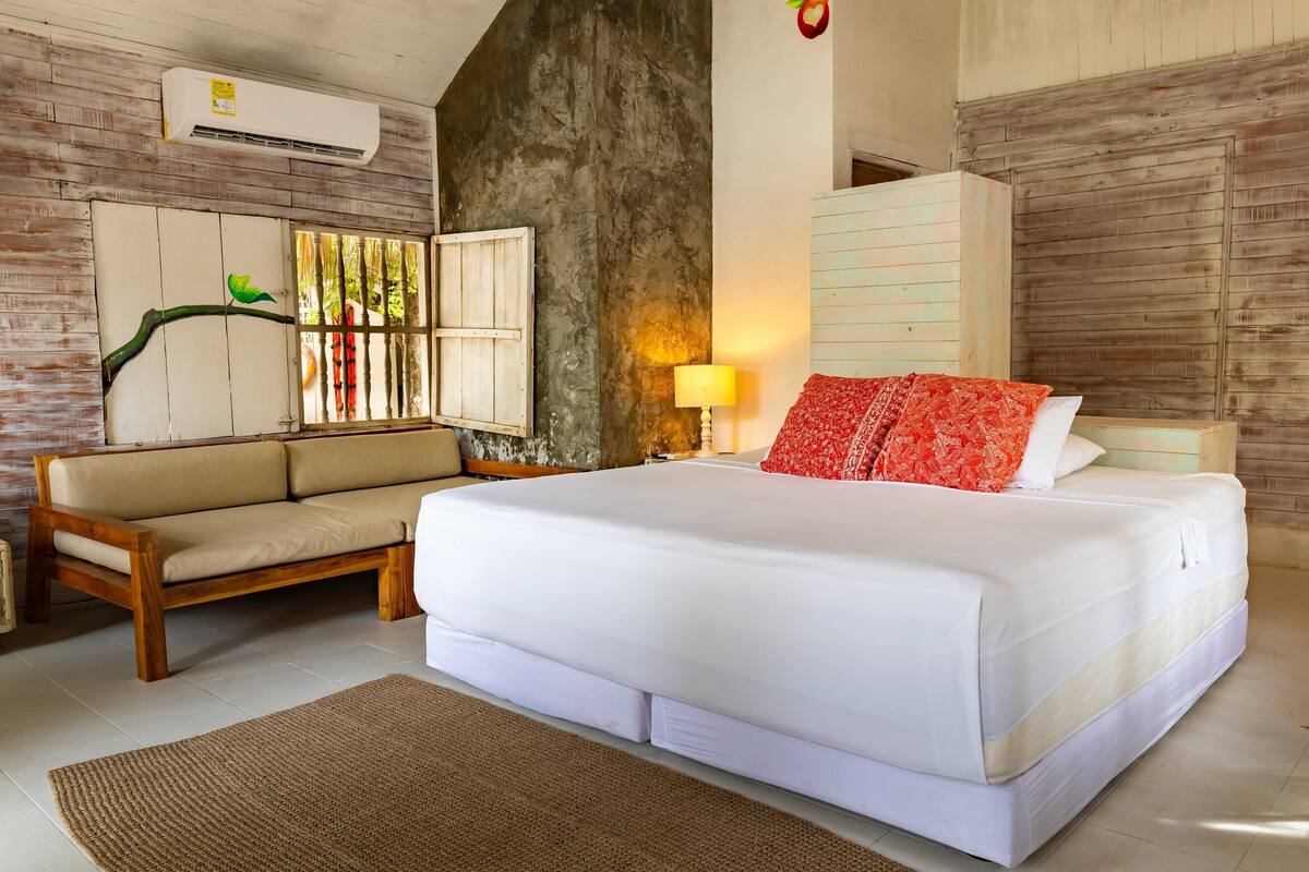 Une chambre à coucher comprenant un lit, un canapé, une lampe et un climatiseur fixé au mur.