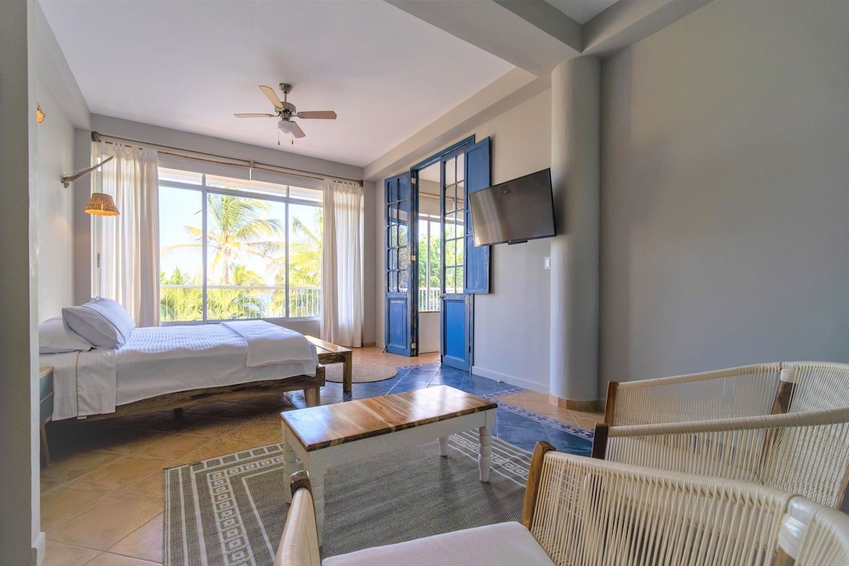 Un dormitorio con cama, escritorio, silla, televisor y balcón con vistas.