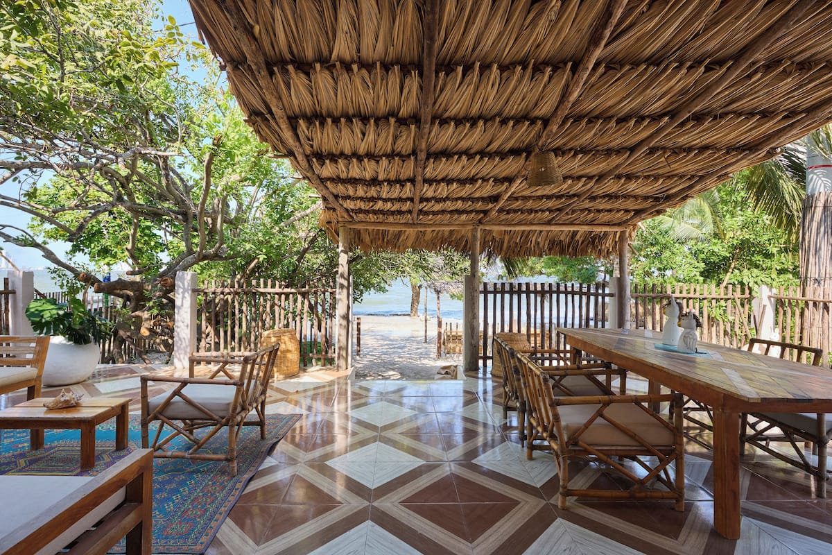 Un espace extérieur abrité, aménagé pour les repas, avec vue sur la plage, du mobilier en bois et un sol à motifs.