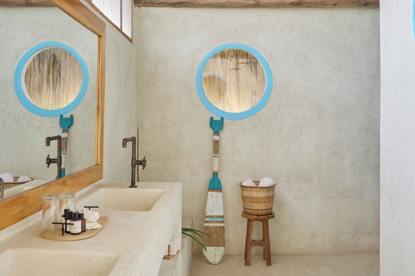 A bathroom with a large mirror, two sinks, a wooden floor, and a broom leaning against the wall.