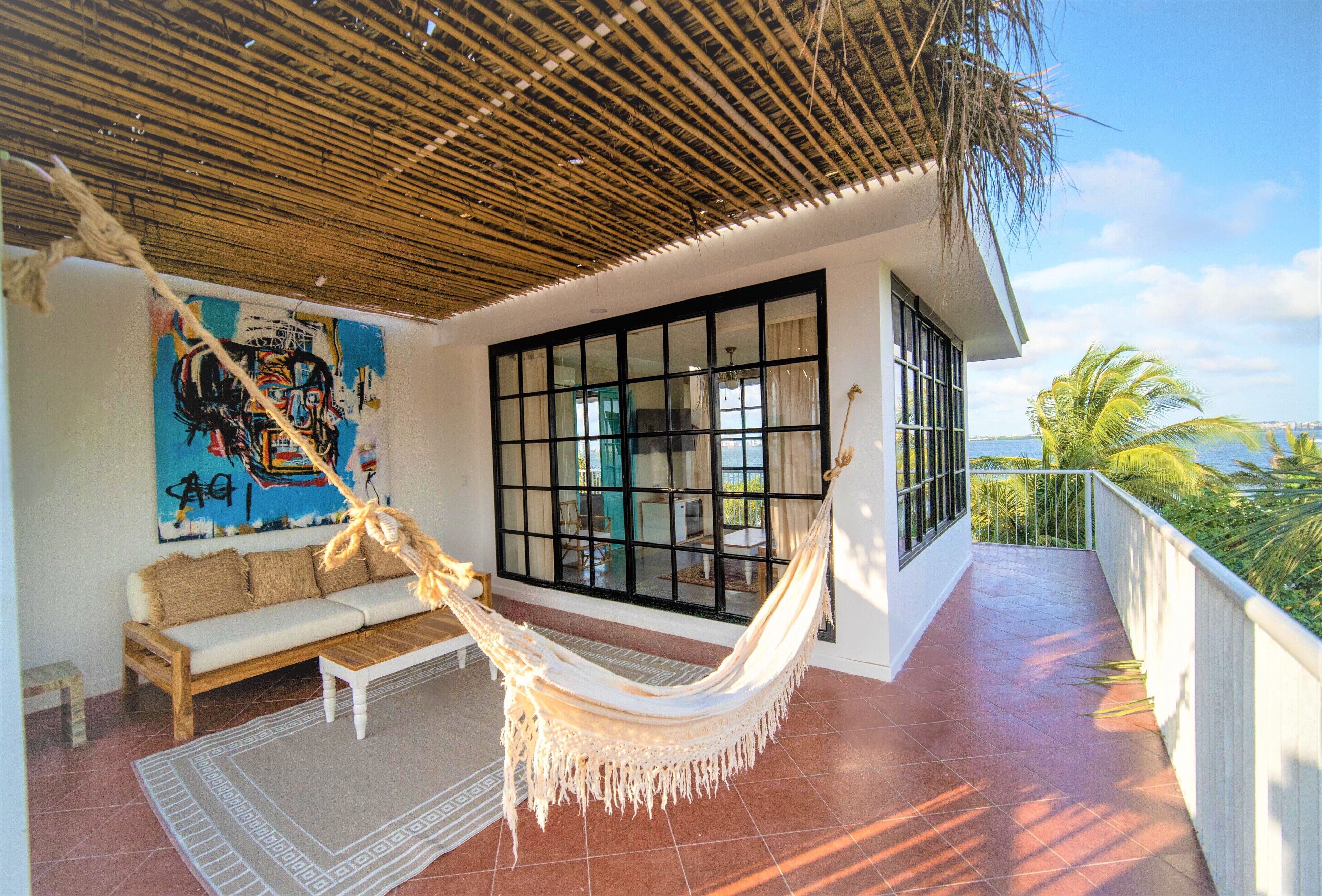 A hammock on a tiled patio with a view of the ocean, a sofa, and a painting on the wall.