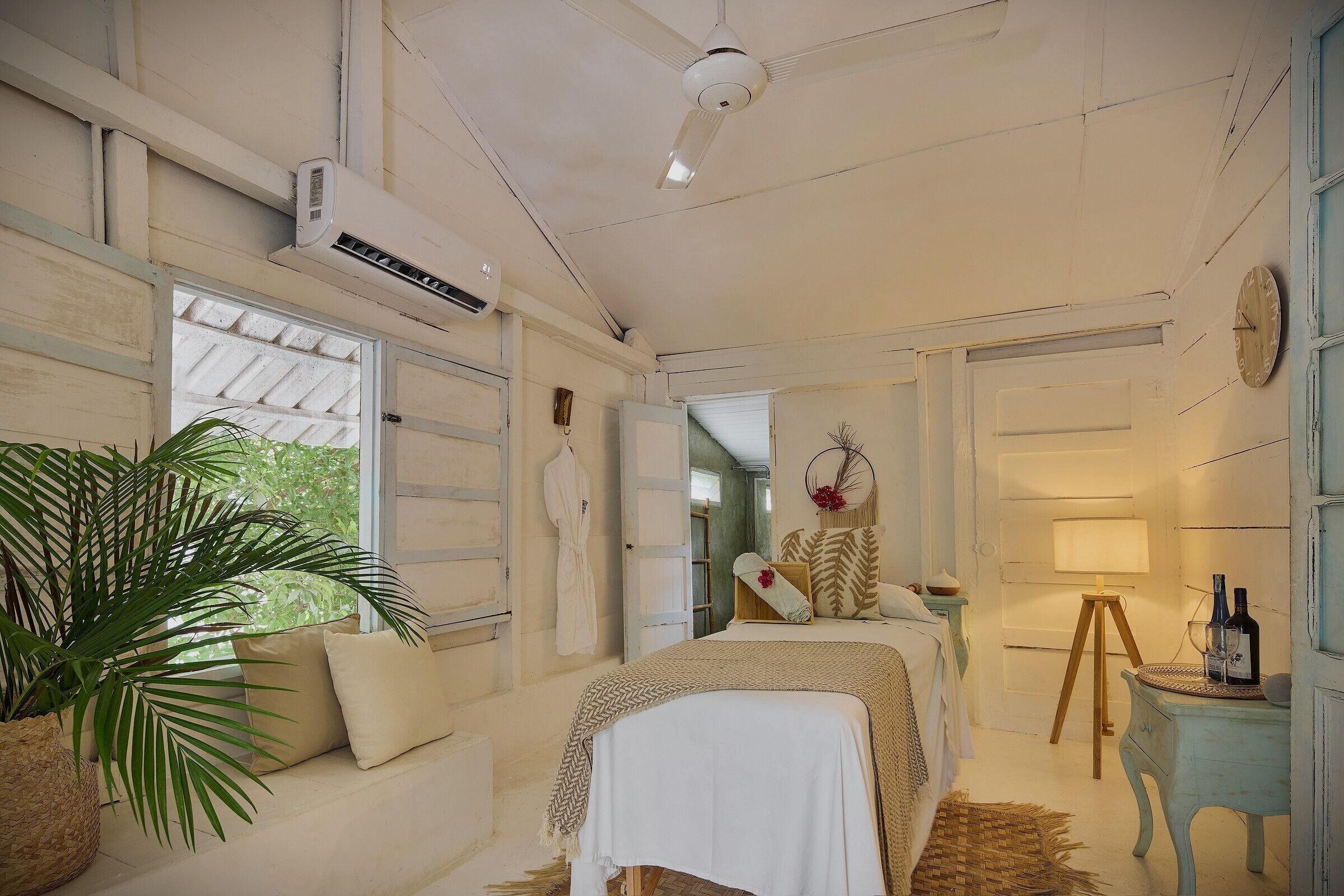 Un dormitorio con una cama, una mesita de noche, una lámpara y una planta grande.