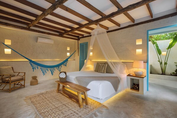 Un dormitorio con una hamaca, una cama con dosel, una mesita de noche y una planta pequeña.