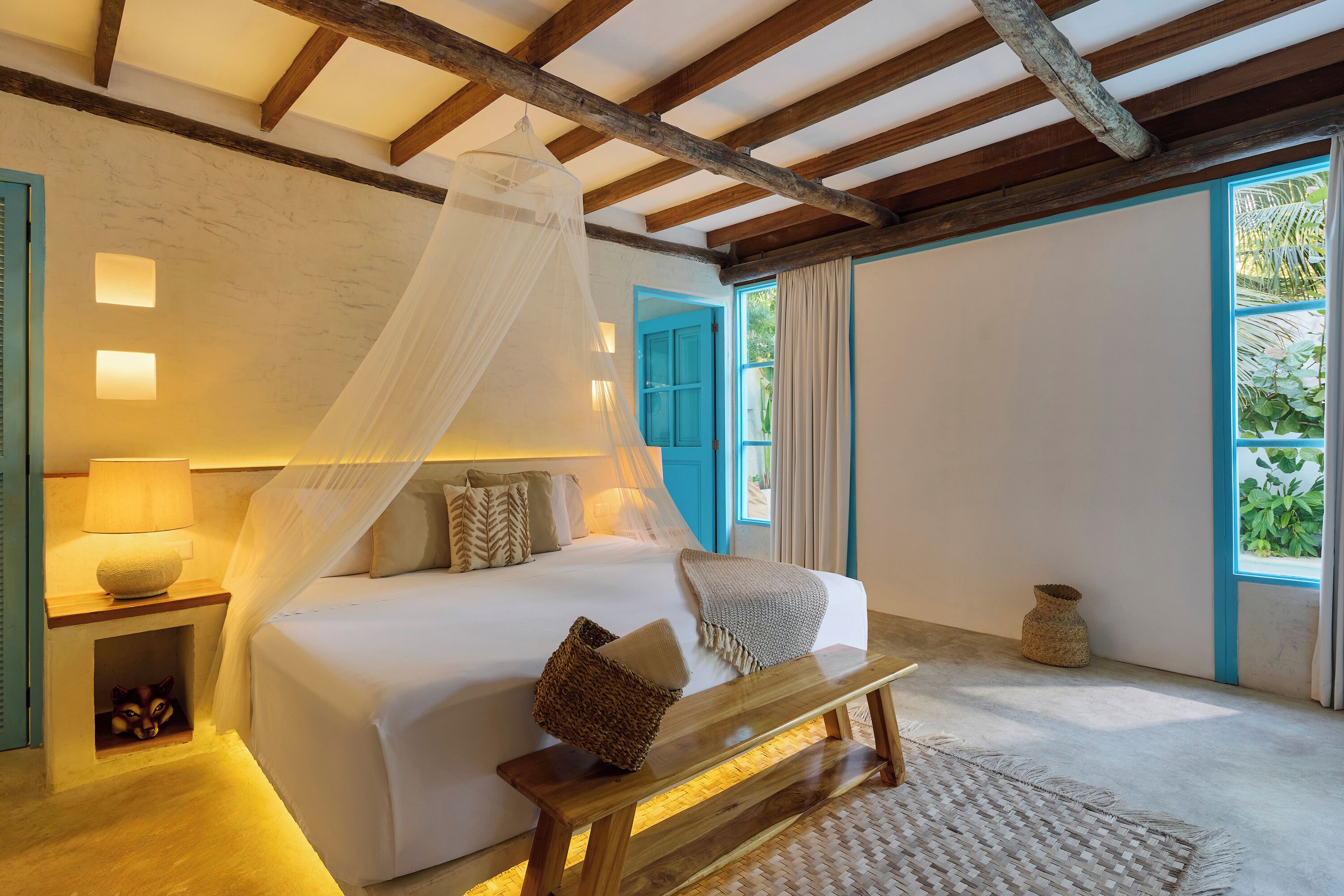 Un dormitorio con cama, mesita de noche, lámpara y un banco.