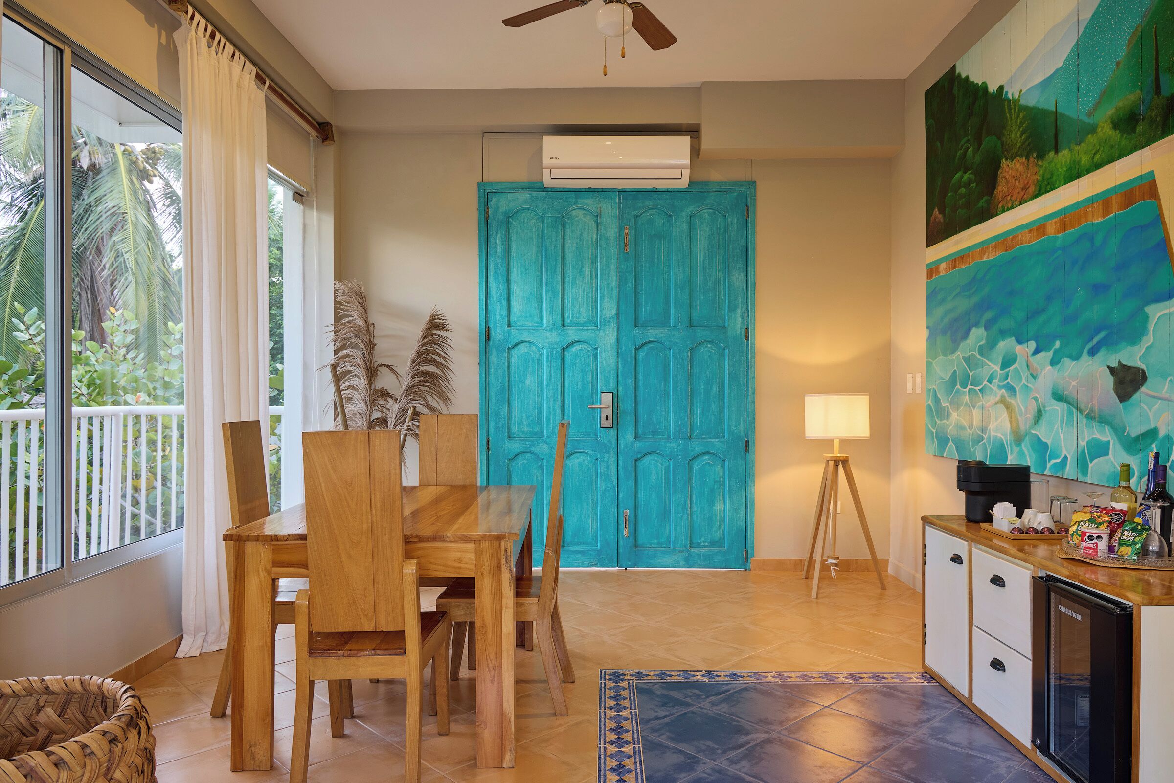 A dining area with a wooden table and chairs, a blue door, and a painting on the wall.