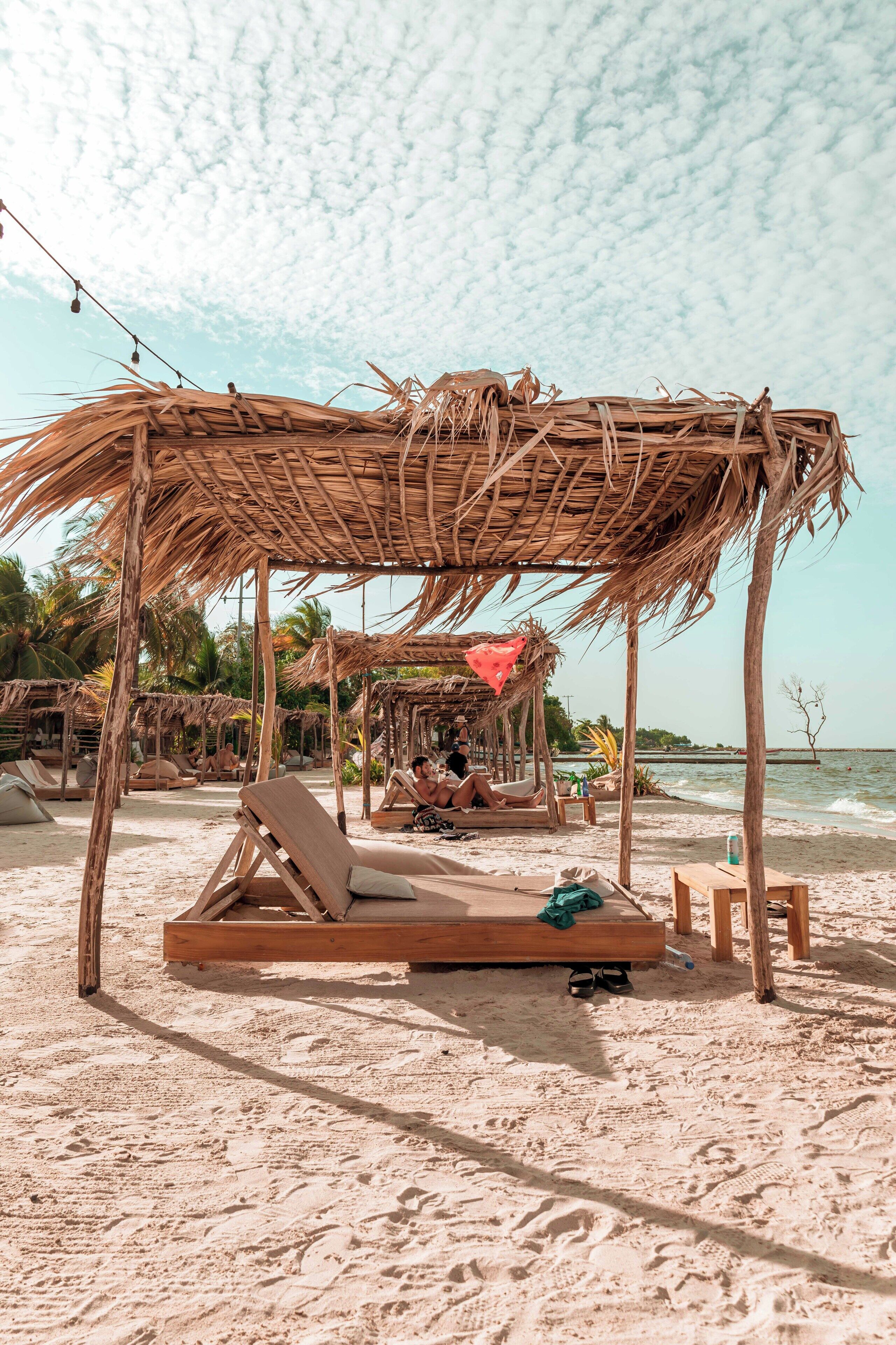 A beach with wooden lounge chairs and thatched umbrellas.