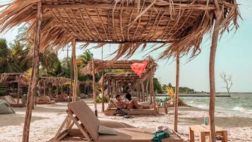 A beach with wooden lounge chairs and thatched umbrellas.