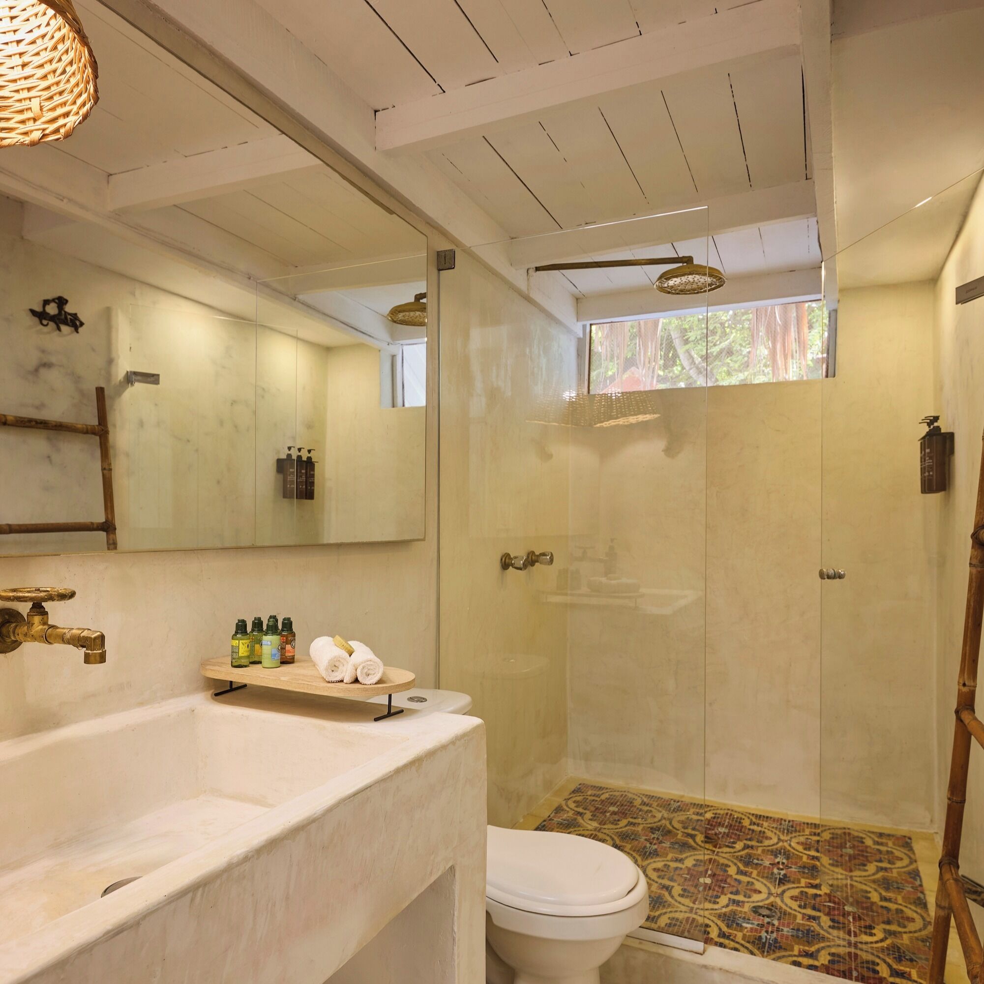 Casa de banho com uma grande pia, sanita e chuveiro. Existem artigos de higiene na pia e um porta-toalhas.