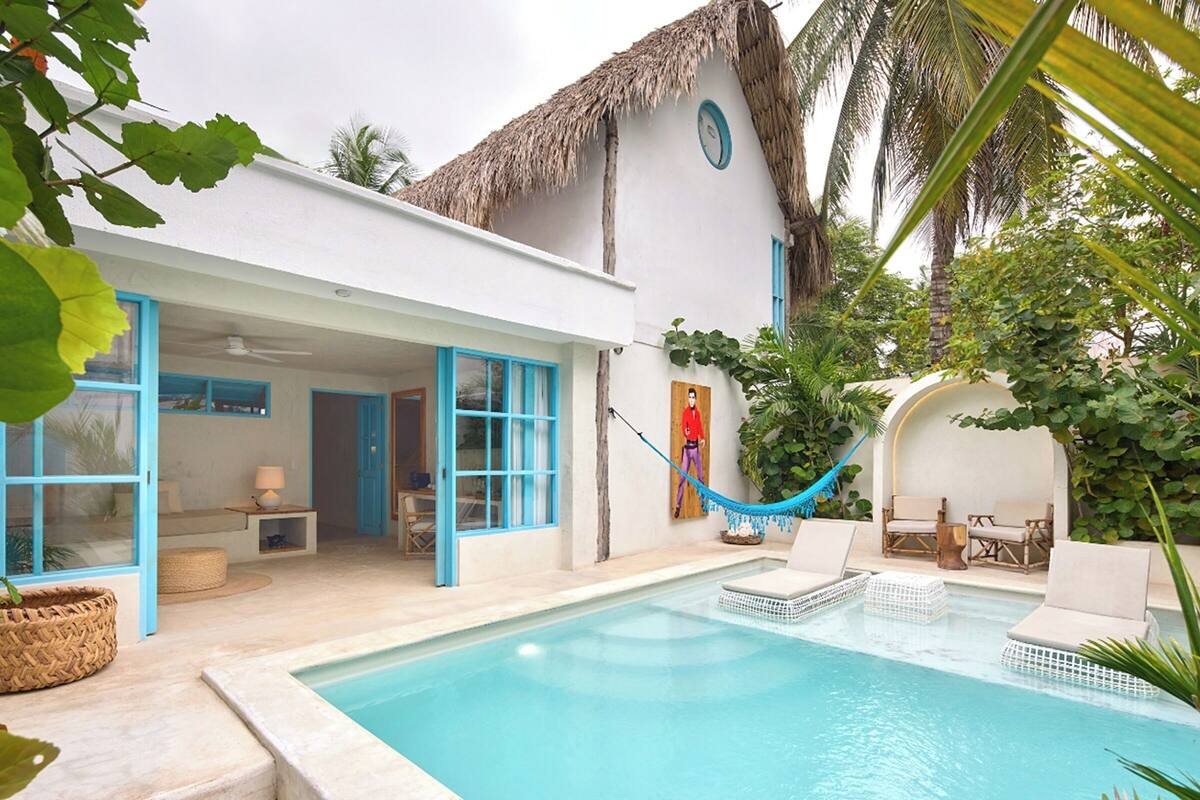 Un espace piscine aménagé avec des chaises longues, un hamac et un bâtiment à toit de chaume.