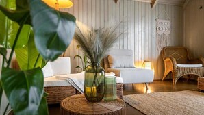 A cozy room with a wicker sofa, a white armchair, and a woven rug. There are two lamps on the wall and a vase with dried plants on a round table. - Green Village Resort (Sfantu Gheorghe)
