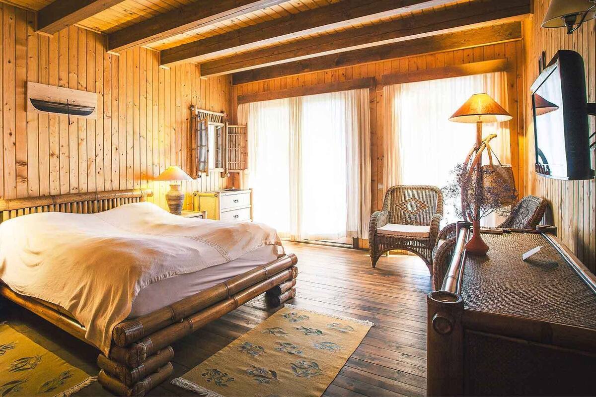 Ein Zimmer in einer Holzhütte mit einem Bett, zwei Lampen, einem Sessel und einem großen Fenster.