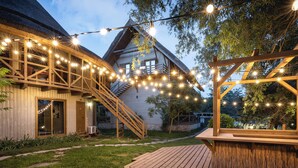 A wooden house with a staircase leading to a deck, surrounded by a garden and string lights. - Green Village Resort (Sfantu Gheorghe)