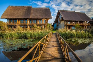 A wooden bridge leading to a building with a thatched roof, surrounded by water and vegetation. - Green Village Resort (Sfantu Gheorghe)