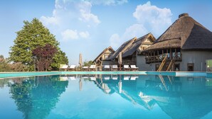 A clear swimming pool with lounge chairs and a thatched-roof building. - Green Village Resort (Sfantu Gheorghe)